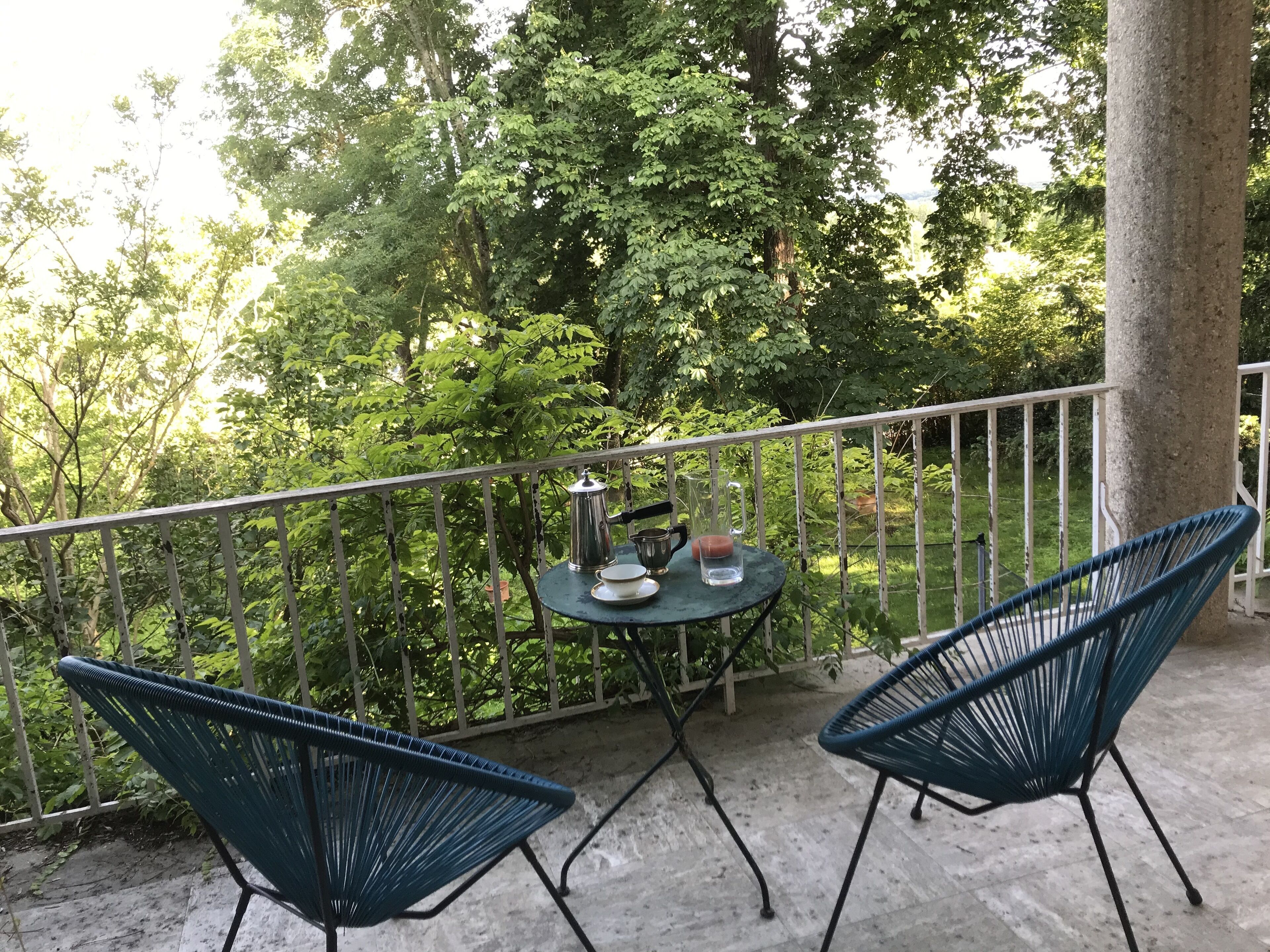 A balcony with two blue chairs, a small round table with a metal pitcher and a glass, and a white railing.
