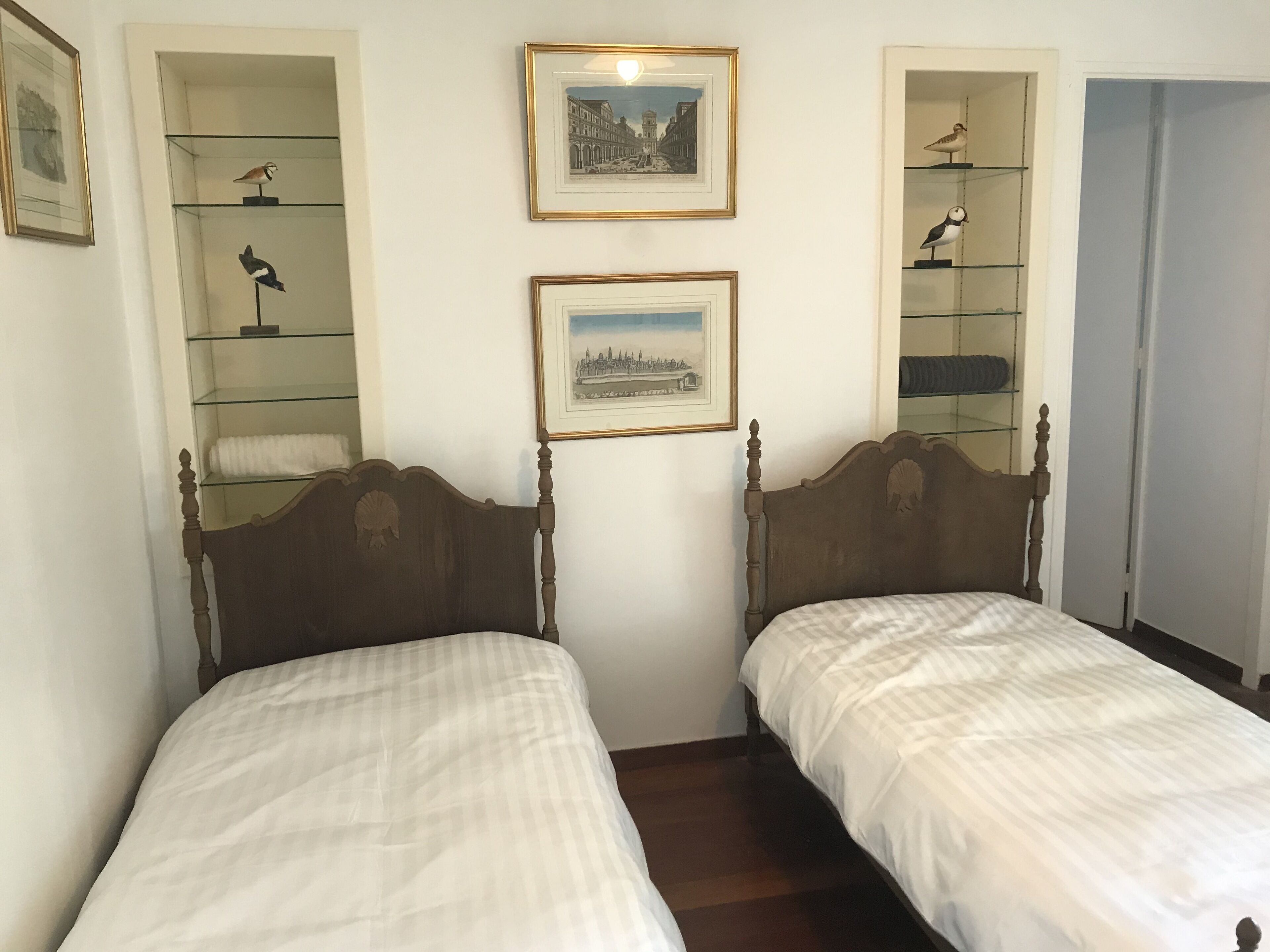 A room with two wooden beds, a framed cityscape picture, and a framed bird illustration on the wall.