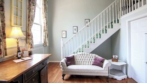 Una habitación con un escritorio de madera, un sofá acolchado, una escalera y una puerta.
