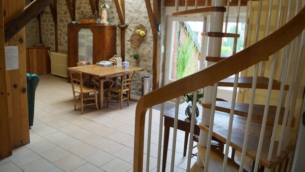 Een rustiek interieur met een houten eettafel en stoelen, een trap met houten leuningen, en stenen muren.