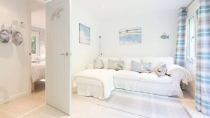 Een slaapkamer met een wit bed, een witte bank en een witte vloer. Er is een deur naar een andere kamer en een raam met een gordijn.