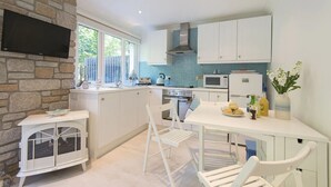 Een moderne keuken met witte kasten, een stenen muur, een inbouwfornuis en een flatscreen televisie boven de aanrecht.