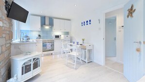 Een moderne keuken met witte kastjes, een ingebouwde oven en een magnetron. Er is een eethoek met een witte tafel en stoelen.