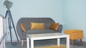 Un salón con un sofá gris, dos cojines color mostaza, una mesita de centro blanca y un sillón naranja pequeño.