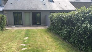 Una casa con tetto a falde, un'entrata principale e un piccolo giardino antistante con un siepe.