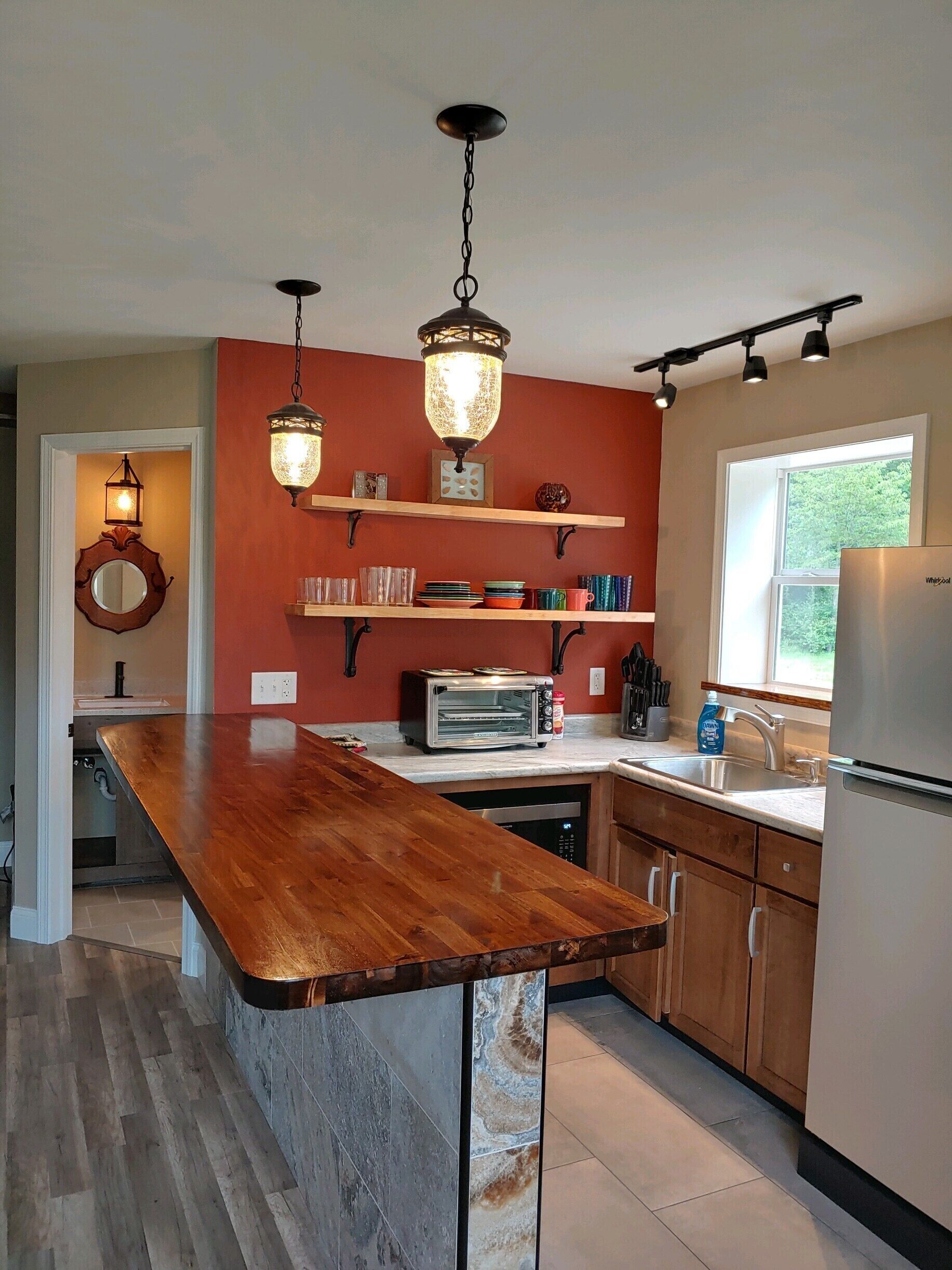 A kitchen with a wooden island, a built-in oven, a refrigerator, and pendant lights.