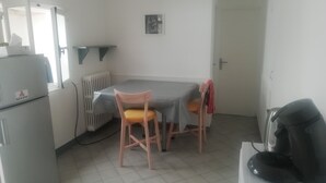 Una habitación pequeña y poco amueblada, con una mesa, dos sillas, un radiador, un refrigerador y una puerta.
