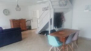 Un comedor con una mesa y sillas de madera, una escalera y una sala de estar con un sofá y un reloj en la pared.
