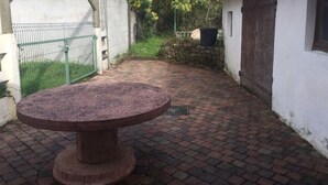 Una mesa redonda de piedra en un patio con suelo de ladrillo, rodeada por un muro blanco y una reja de metal.