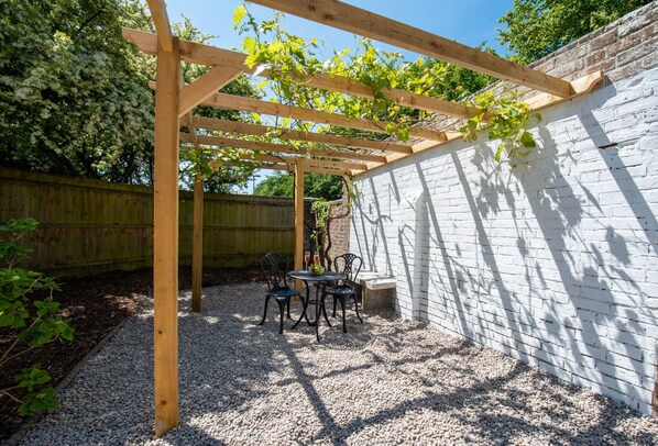 A wooden pergola with vines, a gravel patio, and a white brick wall. - Southgate Coach House - Dorchester (Dorchester)
