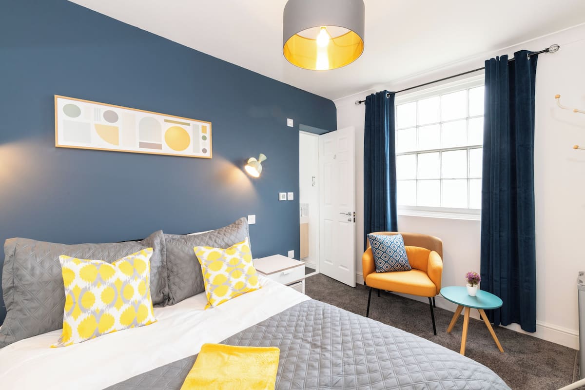 A bedroom with a bed, a chair, a small table, and a window with curtains.