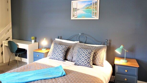 A bedroom with a bed, a desk, a chair, and a nightstand with a lamp. - Bricksage Rooms, King's Lynn South Gate (King's Lynn)