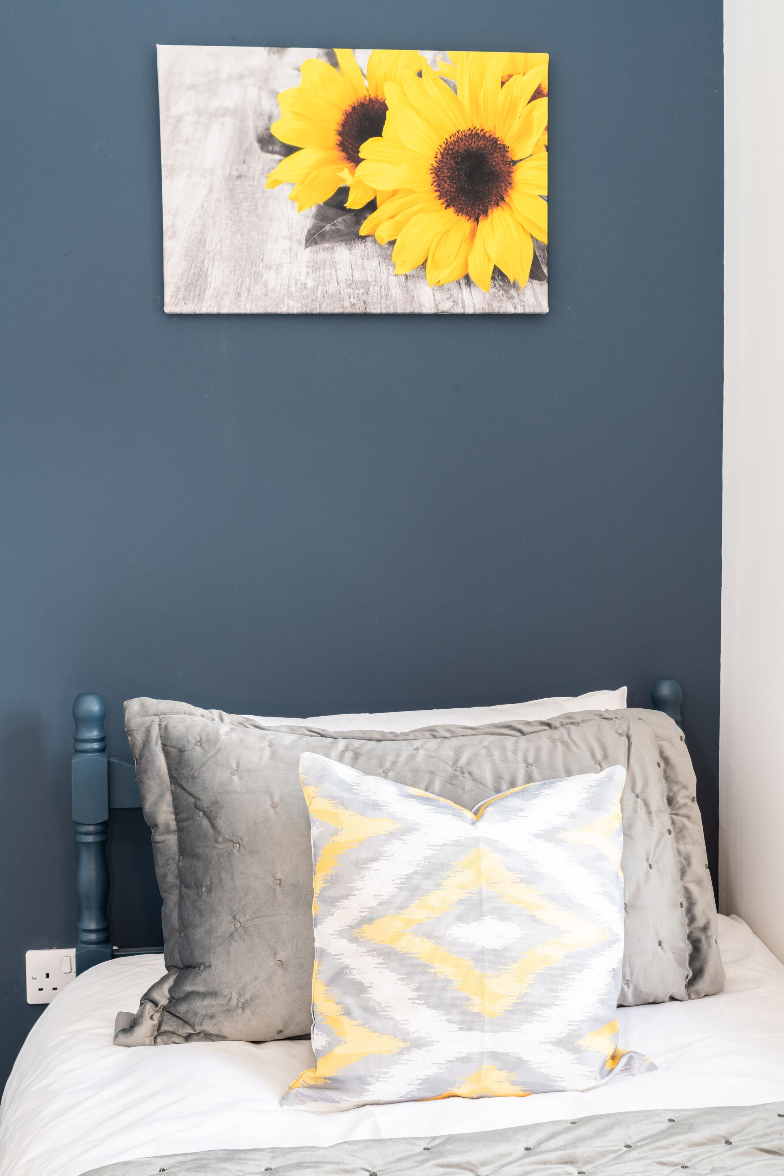 A bedroom with a bed, pillows, and a wall-mounted picture of sunflowers.