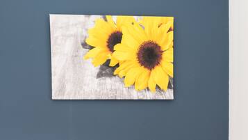 A bedroom with a bed, pillows, and a wall-mounted picture of sunflowers.