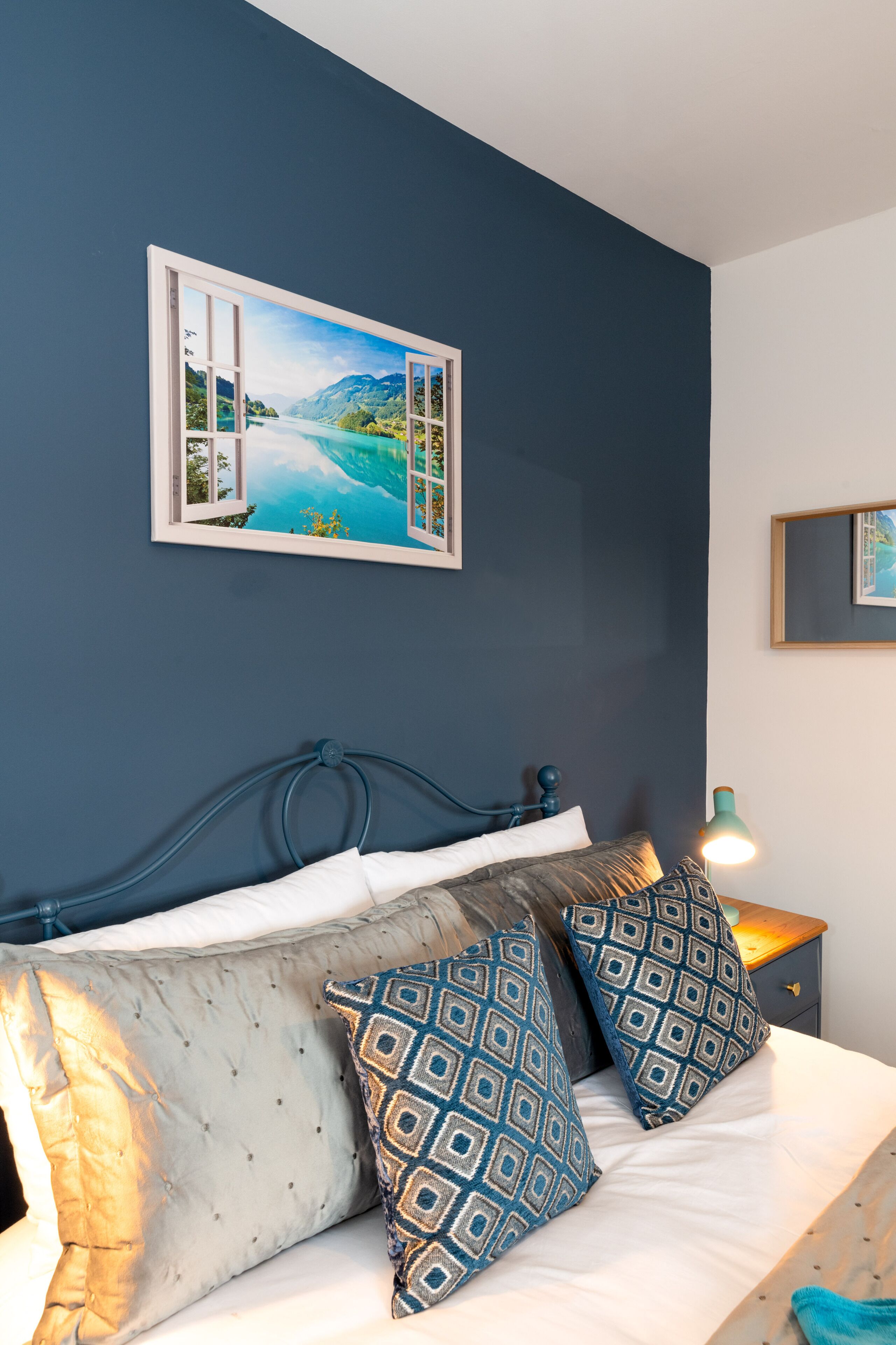 A bedroom with a bed, pillows, a nightstand, a lamp, and a framed picture on the wall.