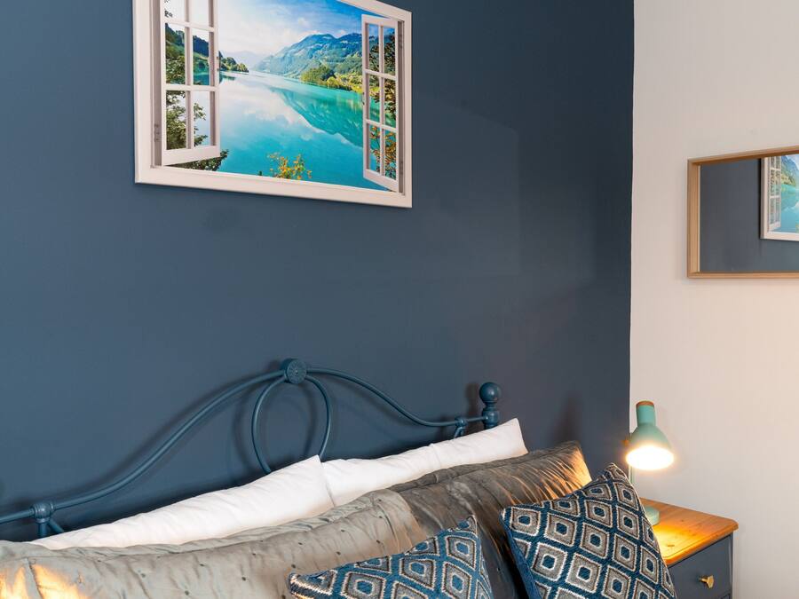 A bedroom with a bed, pillows, a nightstand, a lamp, and a framed picture on the wall.