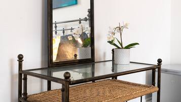 Un espejo con marco negro, una silla de mimbre con asiento y respaldo trenzado, y una orquídea en maceta sobre una mesa blanca.