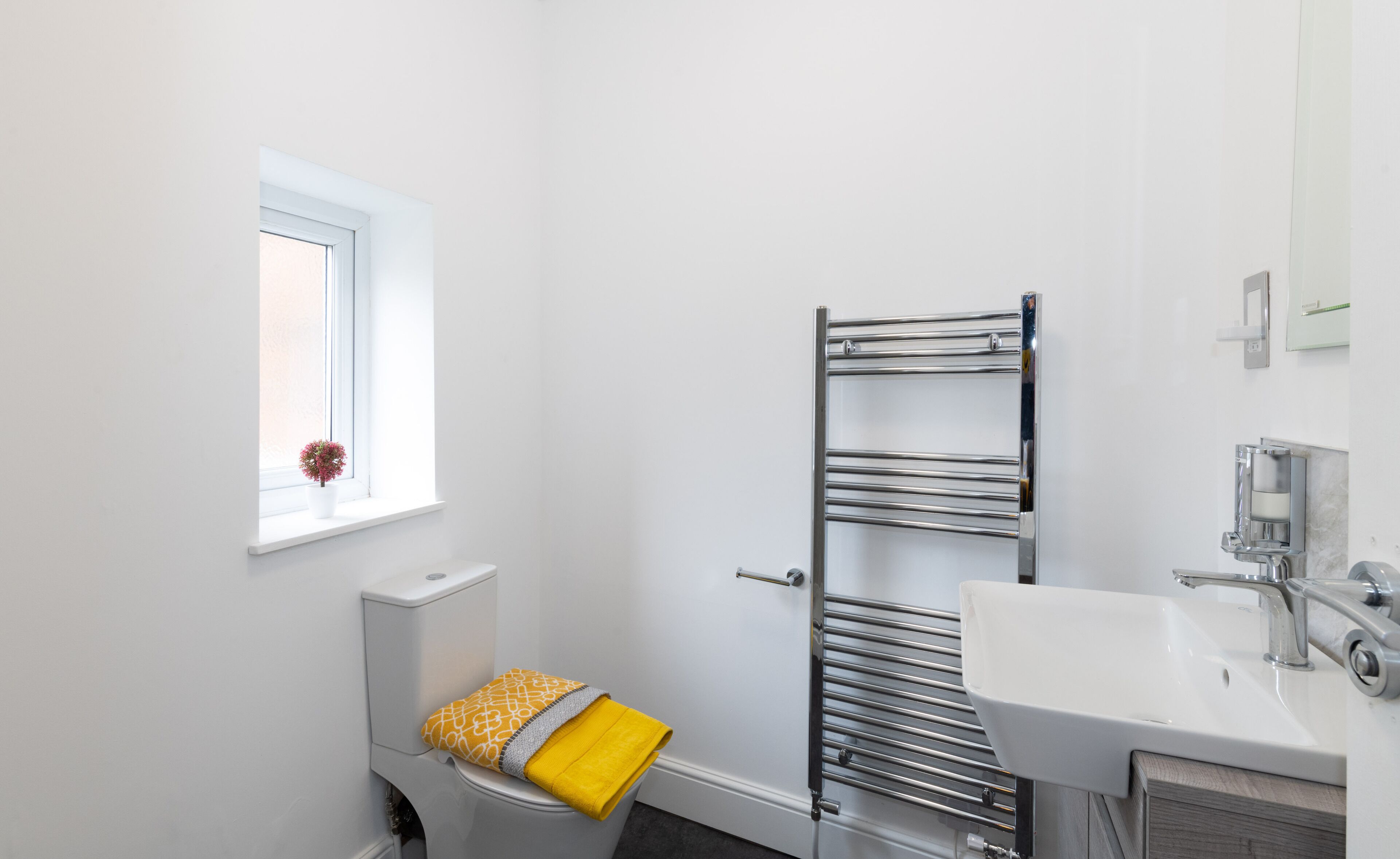 Un baño moderno con inodoro, toallero, lavamanos y ventana.