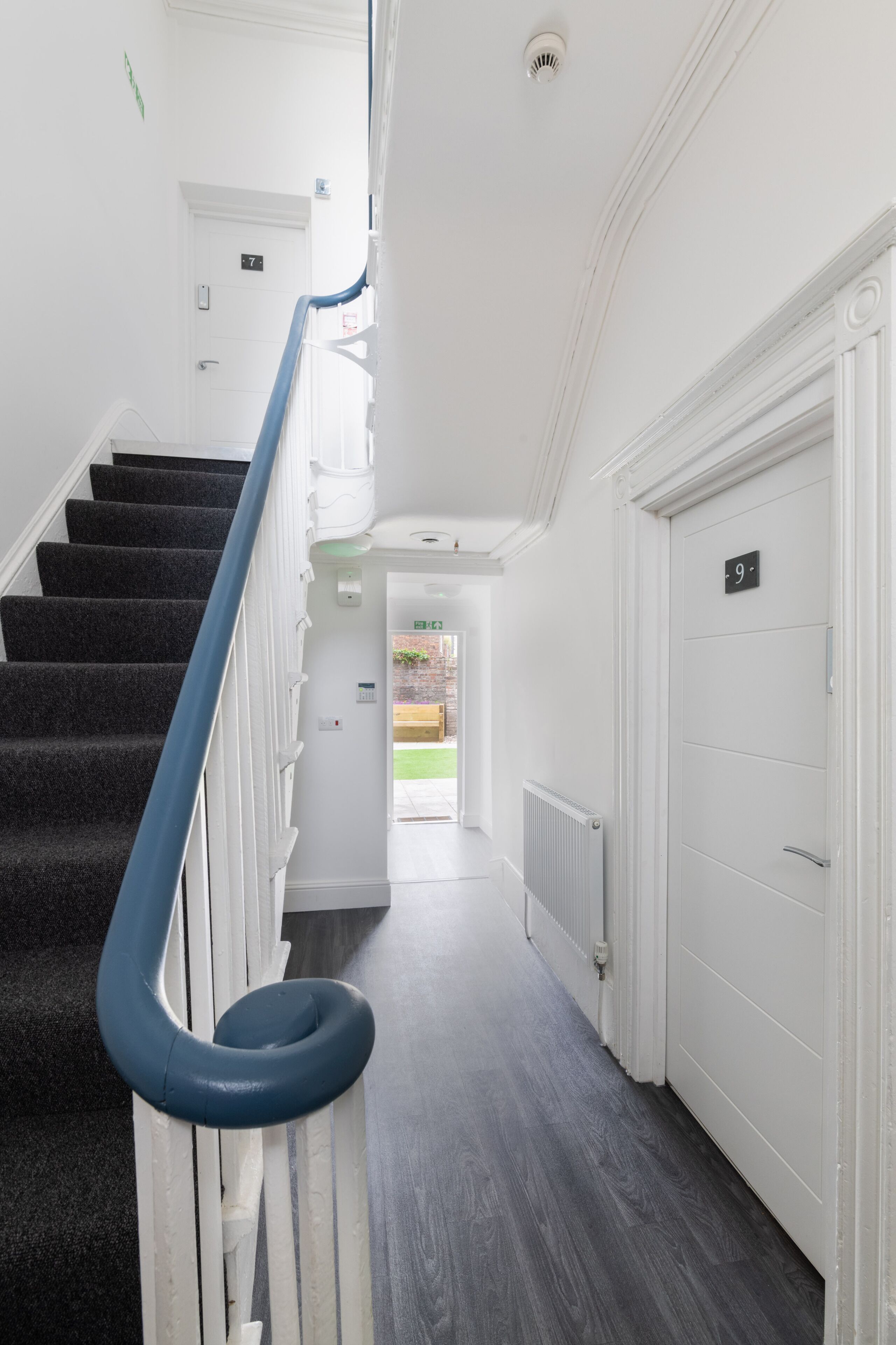 A clean, modern hallway with a carpeted staircase, white walls, and a door marked with the number 9.