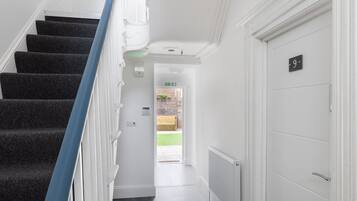 A clean, modern hallway with a carpeted staircase, white walls, and a door marked with the number 9.