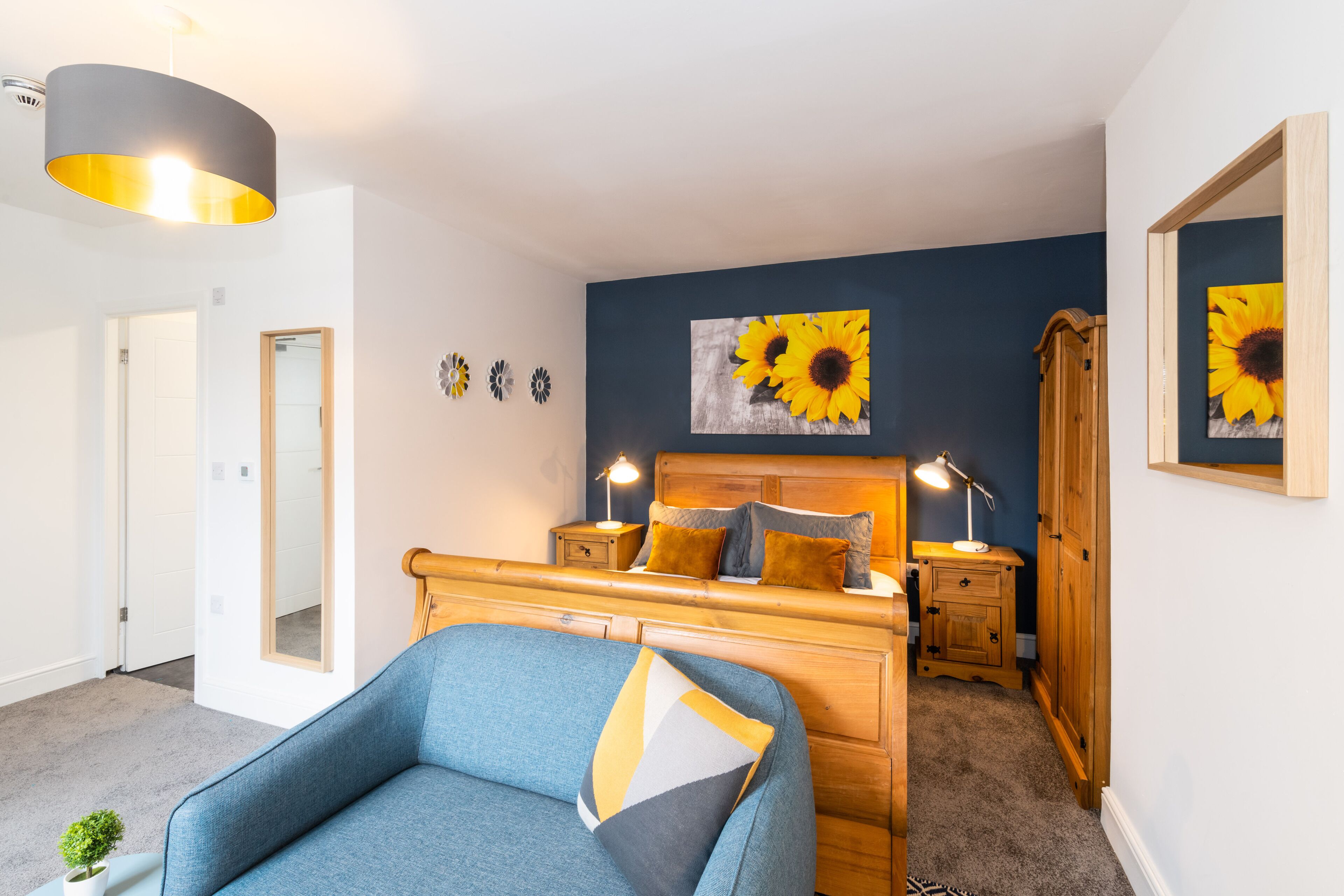 A bedroom with a bed, bedside tables, a lamp, a mirror, and a wall with a sunflower painting.