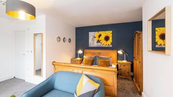 A bedroom with a bed, bedside tables, a lamp, a mirror, and a wall with a sunflower painting.