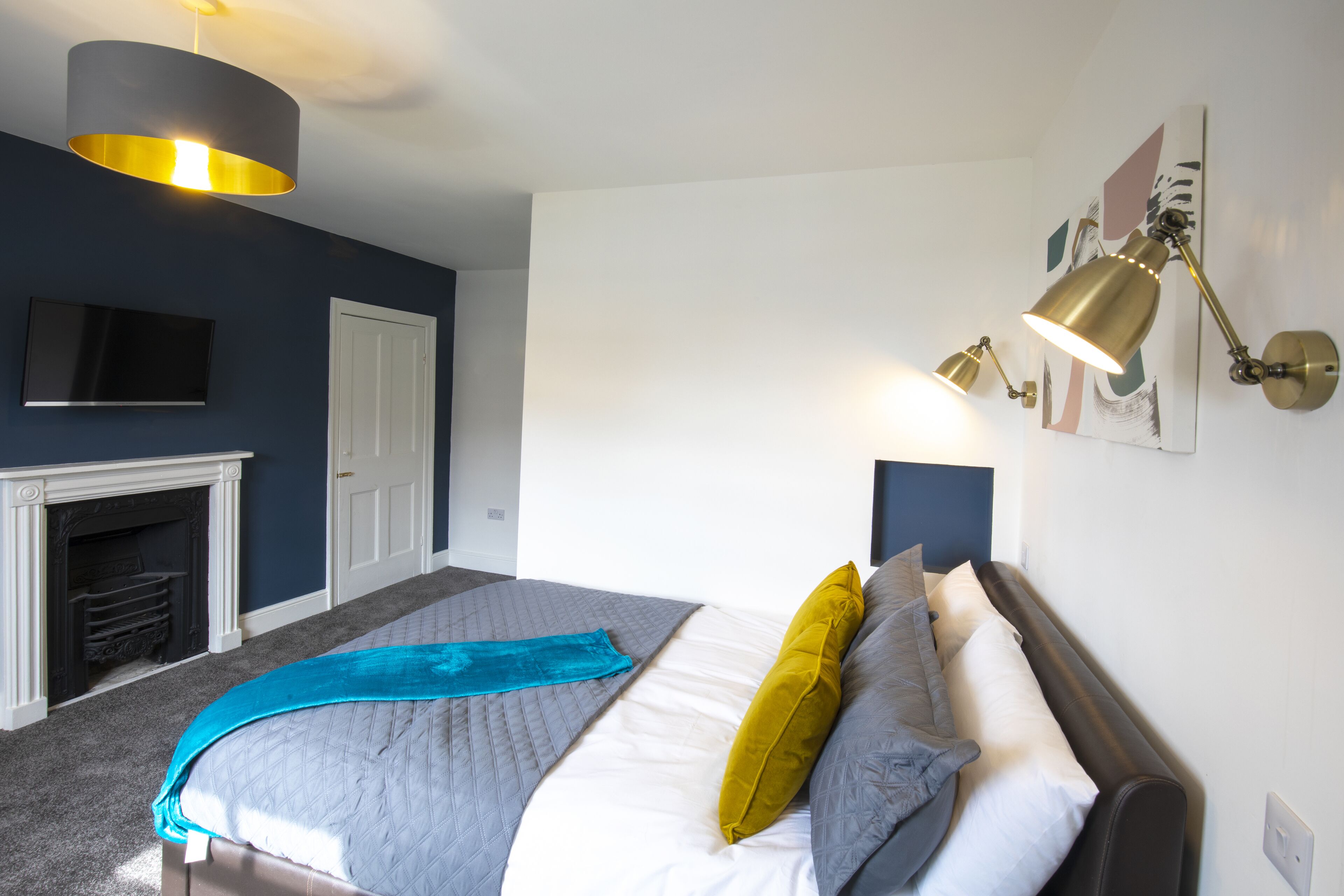 A bedroom with a bed, a fireplace, a mounted TV, and wall-mounted lamps.