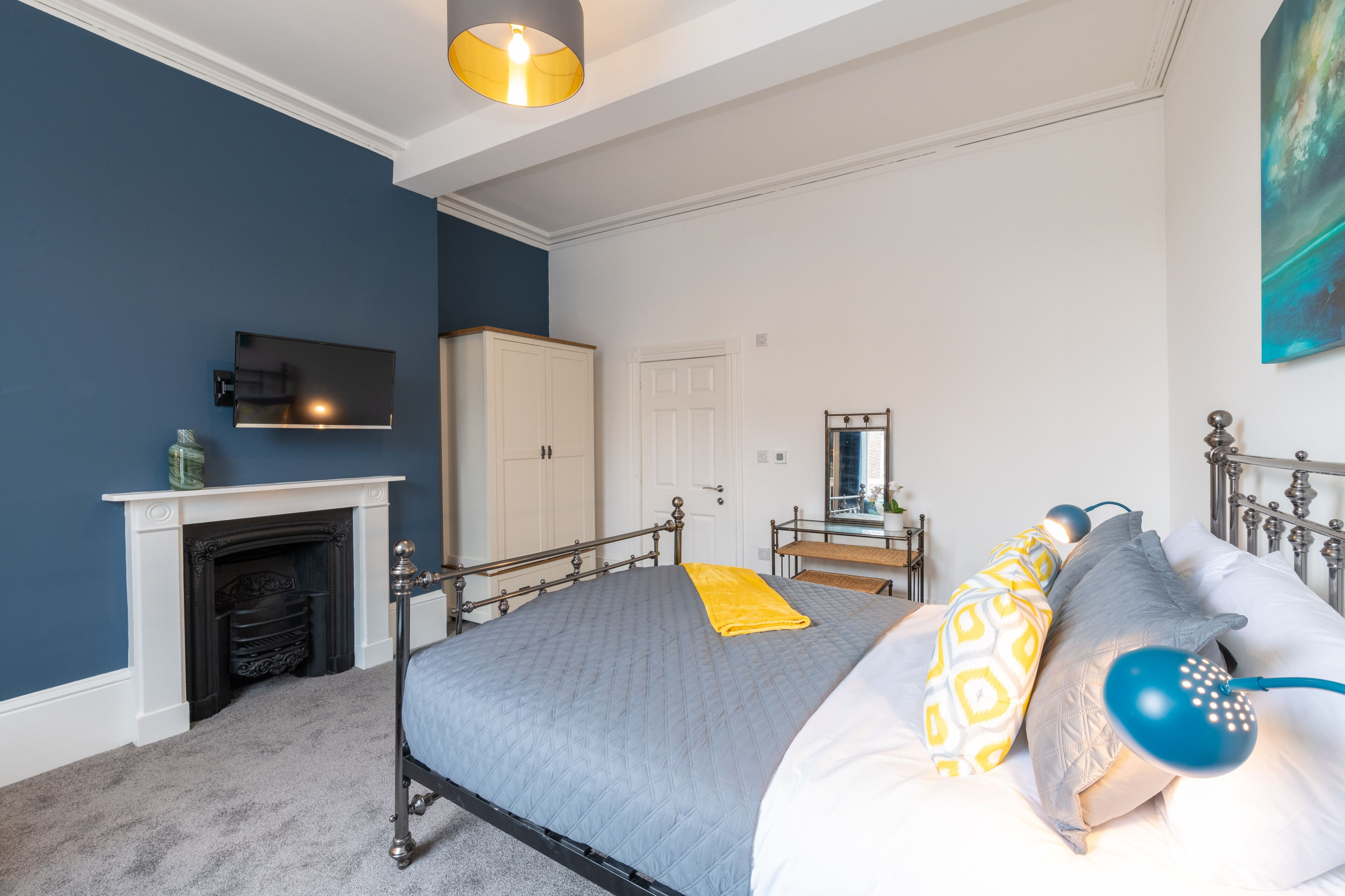 A bedroom with a bed, a television, a fireplace, a wardrobe, and a mirror.