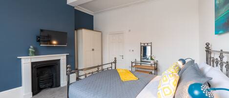 A bedroom with a bed, a television, a fireplace, a wardrobe, and a mirror.