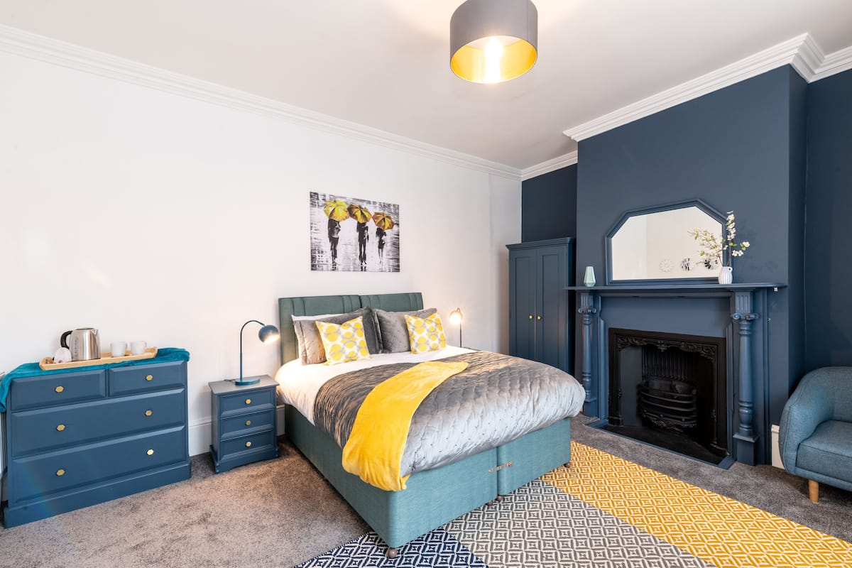A bedroom with a bed, dresser, nightstand, and a fireplace.