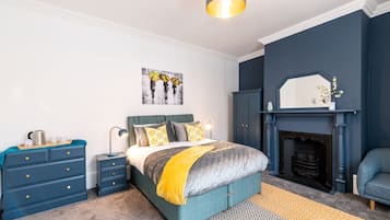 Een slaapkamer met een bed, een kaptafel, nachtkastje en een open haard.