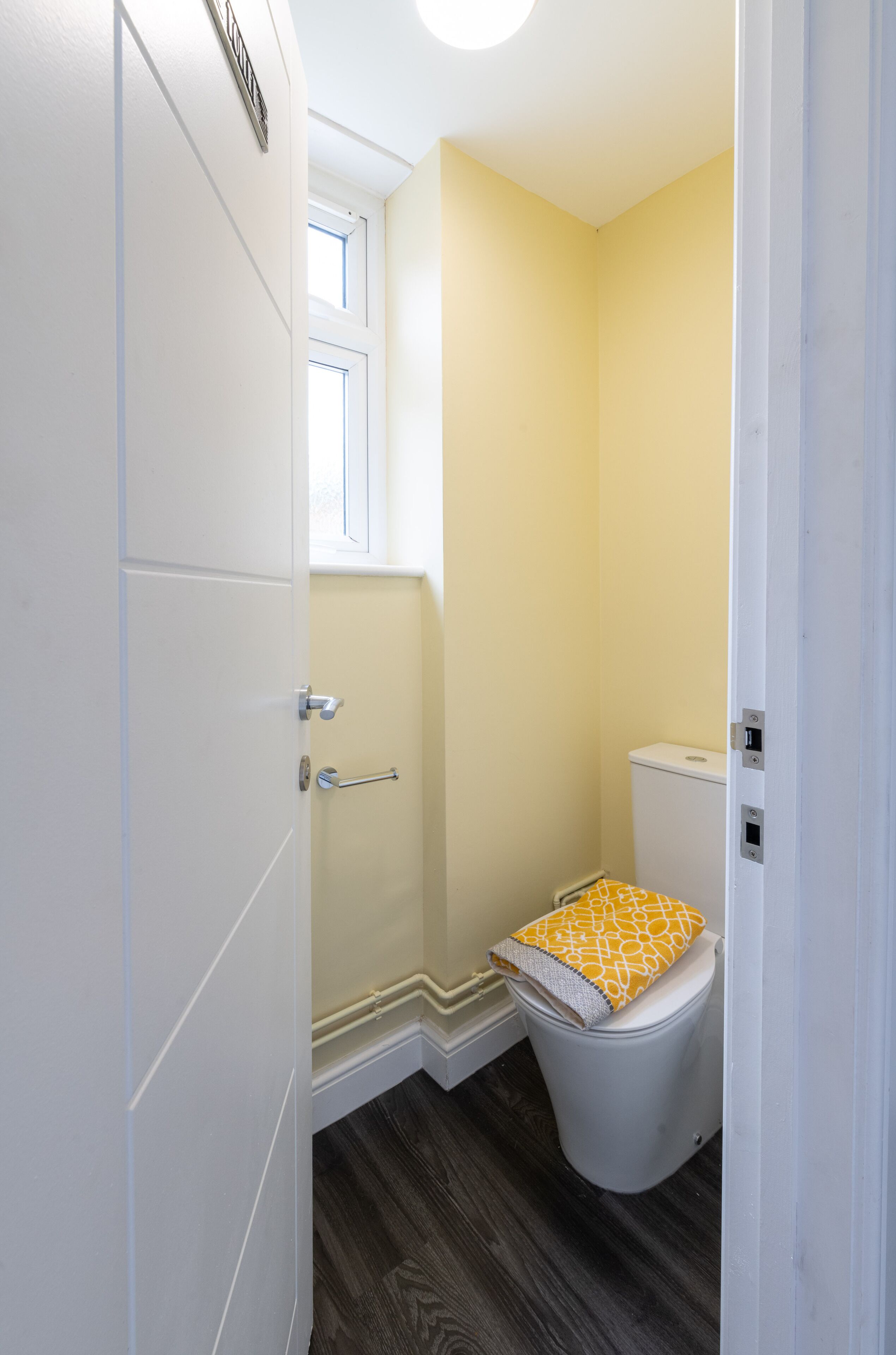A small bathroom with a toilet, a white door, and a window.