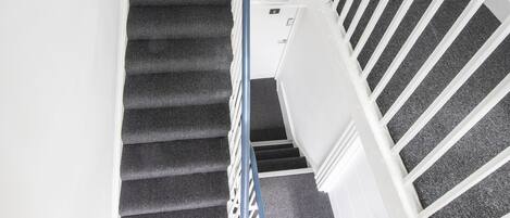 A staircase with a handrail, carpeted steps, and white walls.