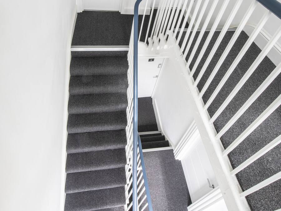 Una escalera con barandilla, escalones alfombrados y paredes blancas.