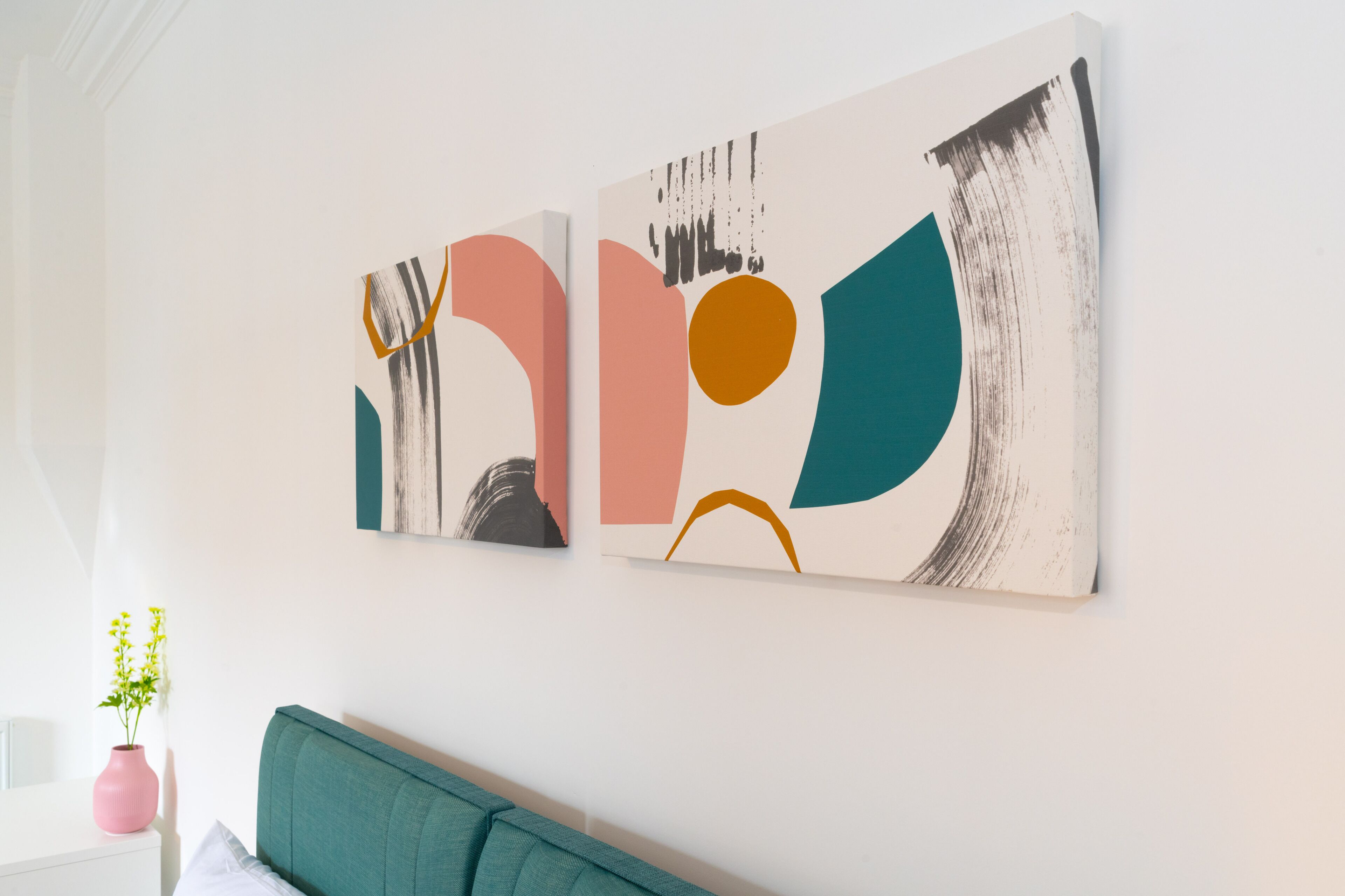Une pièce avec un canapé de couleur turquoise, une table de chevet blanche ornée d’un vase rose et des œuvres d’art abstraites accrochées au mur.