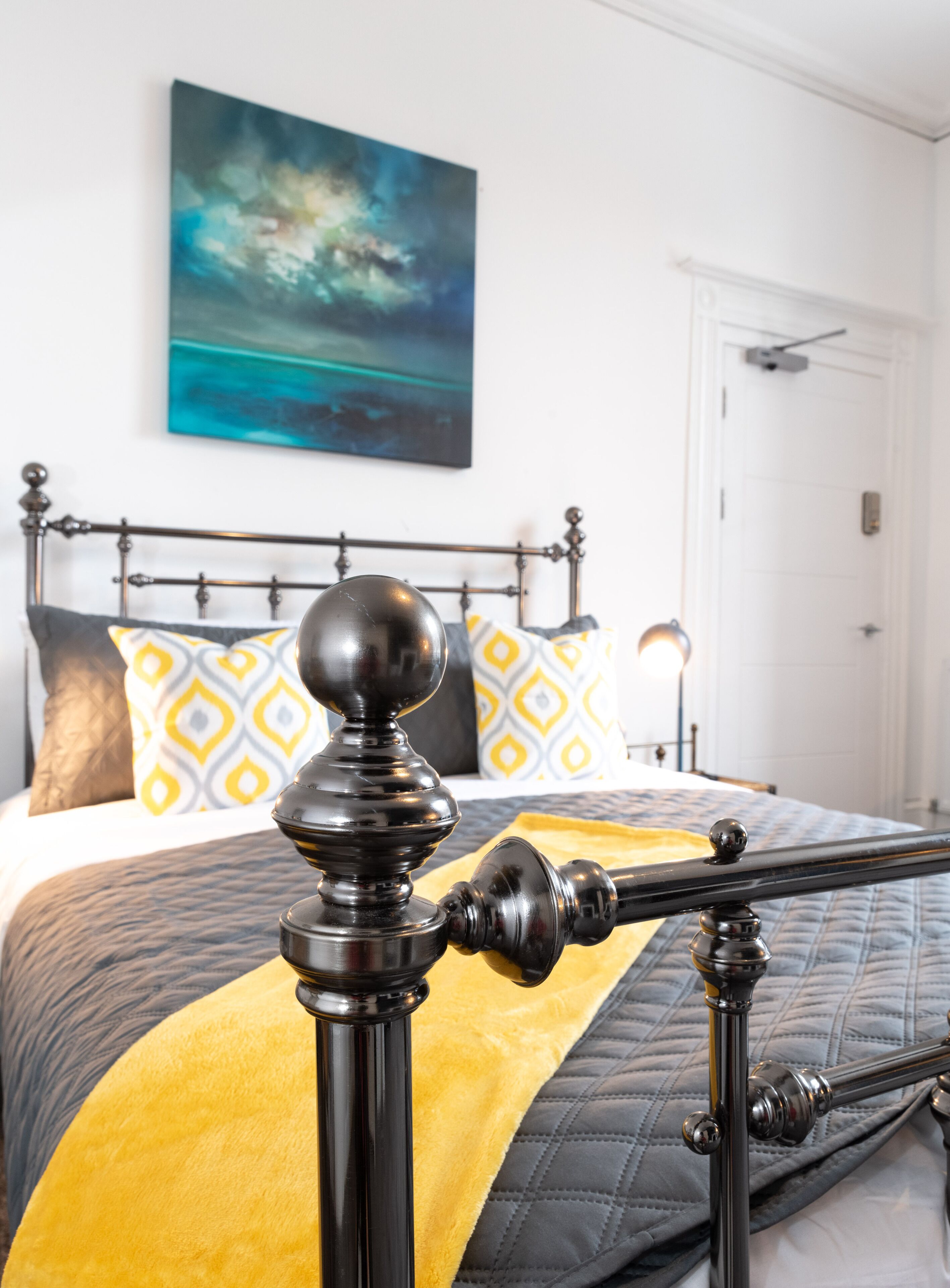 A bed with a metal frame, a yellow throw blanket, and patterned pillows.