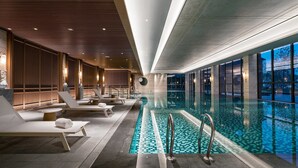 Une piscine intérieure moderne, dotée de chaises longues et offrant une vue sur le ciel nocturne.