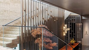 Un intérieur moderne agrémenté d’un escalier, d’un banc en bois et d’un arbre décoratif.