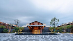 Un bâtiment moderne doté d’un style architectural traditionnel, avec une entrée centrale surmontée d’un toit et entourée d’une cour.
