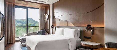 A modern hotel room with a large bed, a view of greenery, and a wooden accent wall.