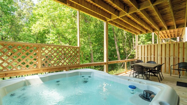 Un jacuzzi en una terraza de madera, con una valla y sillas de madera.