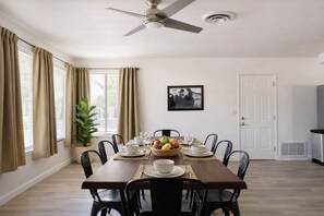 A dining room with a wooden table set for six, surrounded by black chairs. There is a ceiling fan, a window with beige curtains, and a framed picture on the wall. - Private desert retreat on ½ acre with mountain views — stargaze from the fire pit or optional hot tub, relax in hammocks, and enjoy modern comforts just 15–20 minutes from Joshua Tree National Park. (Yucca Valley)