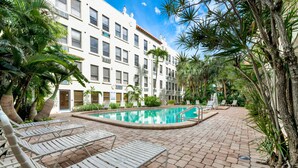 Un espace piscine comprenant des chaises longues, une piscine et un bâtiment doté de nombreuses fenêtres et de balcons.