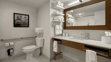 A modern bathroom with a toilet, sink, and mirror. There are towels and a hand dryer on the counter.