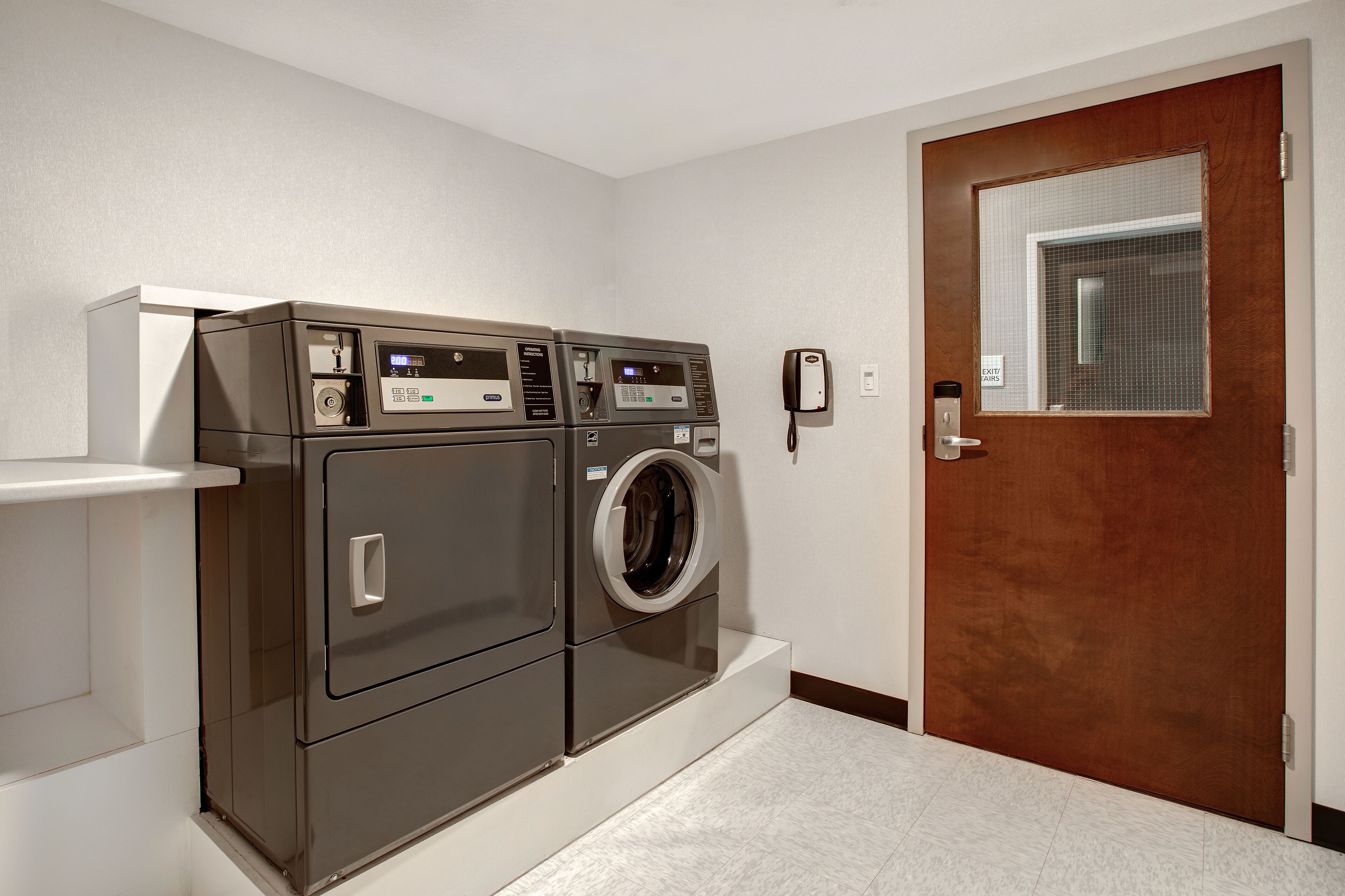 A laundry room with two front-loading washers and dryers, a white sink, and a wooden door with a window.