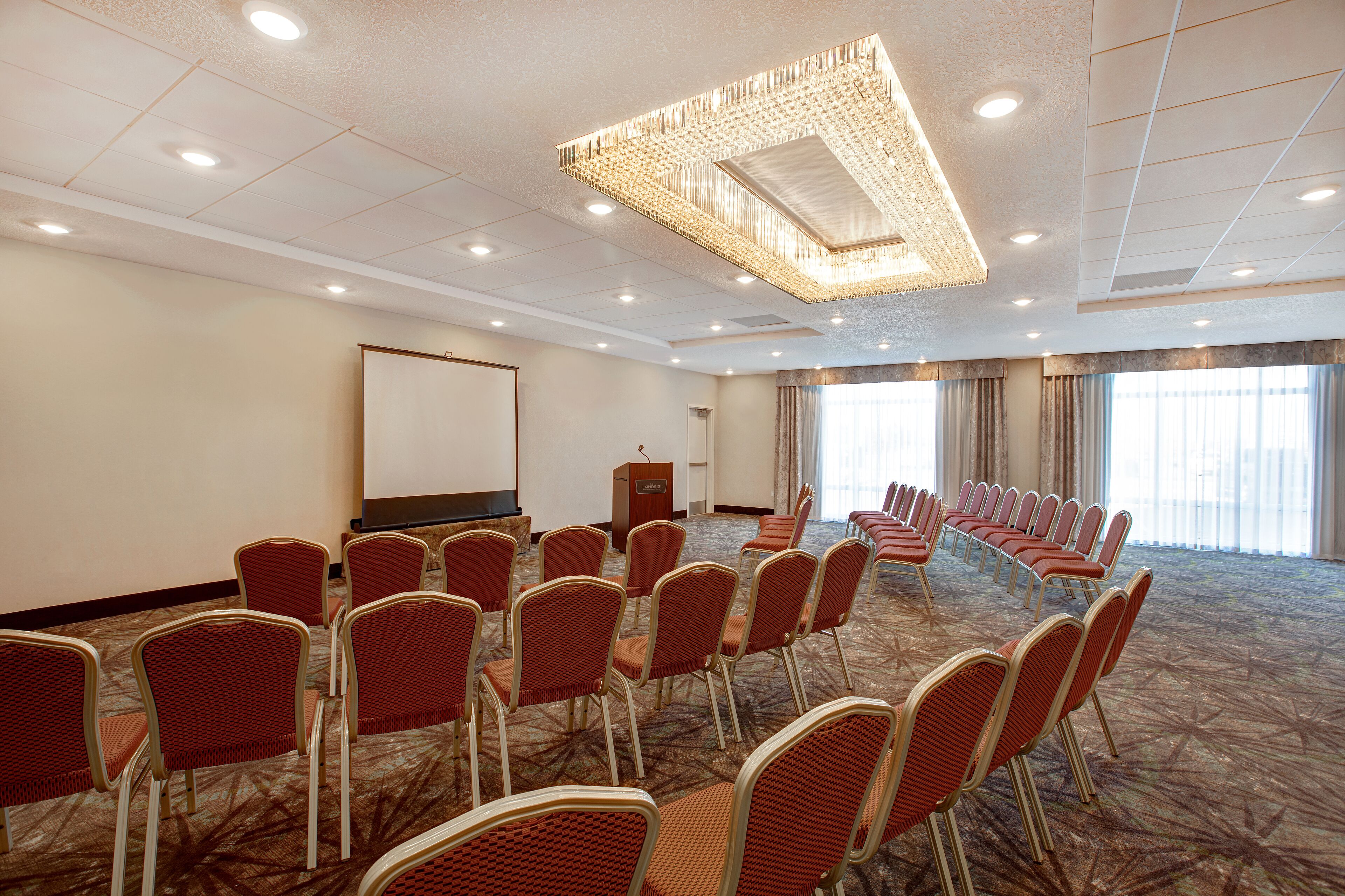 A conference room with rows of chairs, a podium, and a projector screen.