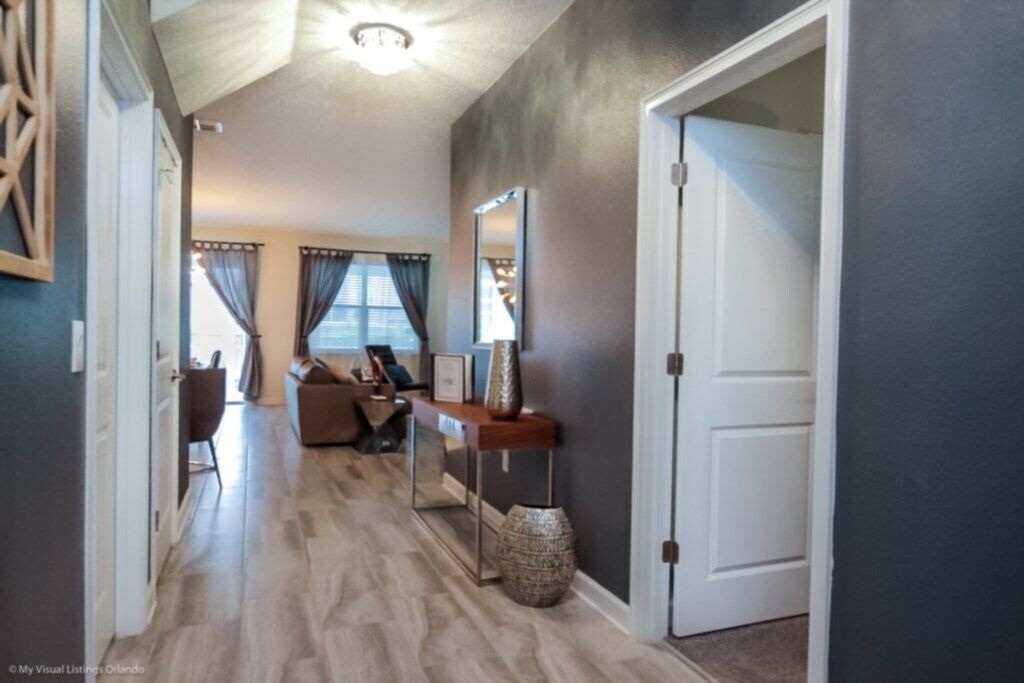 A hallway with a wooden floor, a dark wall, a white door, and a mirror on the wall.