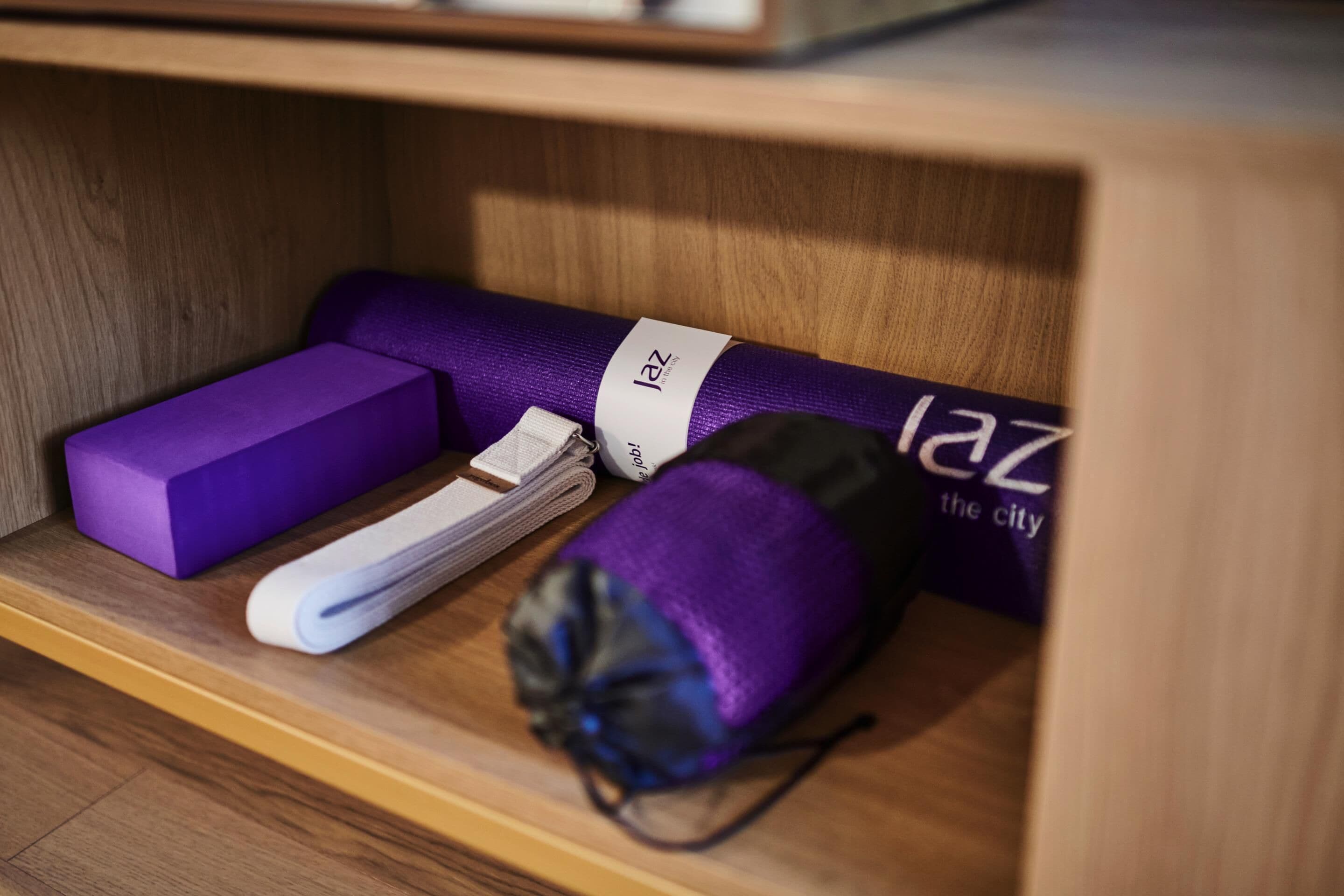 A wooden shelf with a purple yoga mat, a rolled-up towel, and a black bag with a white label.
