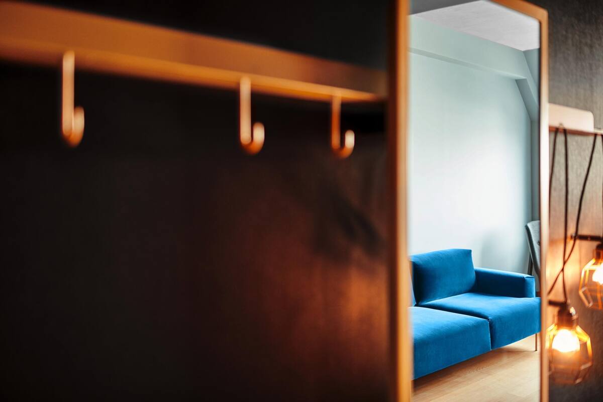 Une pièce avec un canapé bleu, un plancher en bois et un luminaire suspendu.