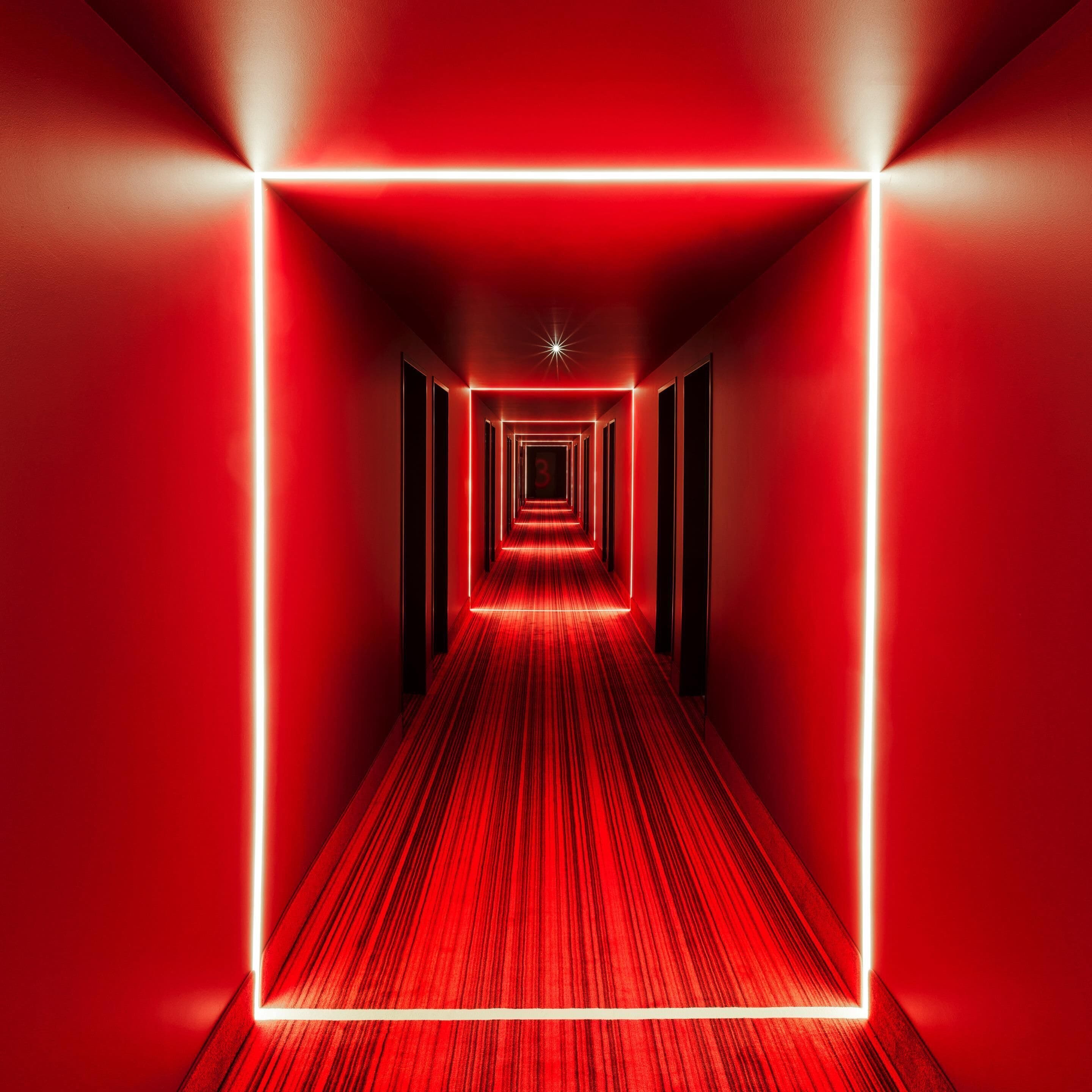 Ein rot beleuchteter Korridor mit Teppichboden und Wandverkleidung, der zu einer sternförmigen Leuchte an der Decke führt.